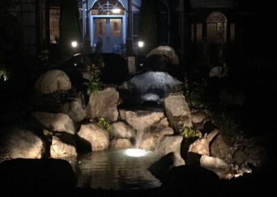 Night time view of House with a large rock fountain and pond in front